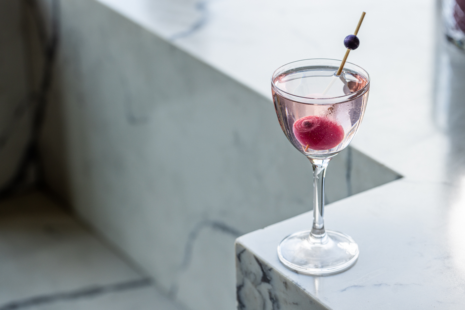 a gibson cocktail with a red pickled onion on a white marble surface
