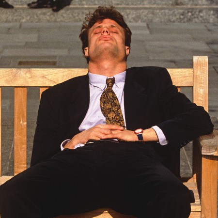 Man in business attire napping on a bench during the afternoon, symbolizing midday fatigue or energy slump at work.
