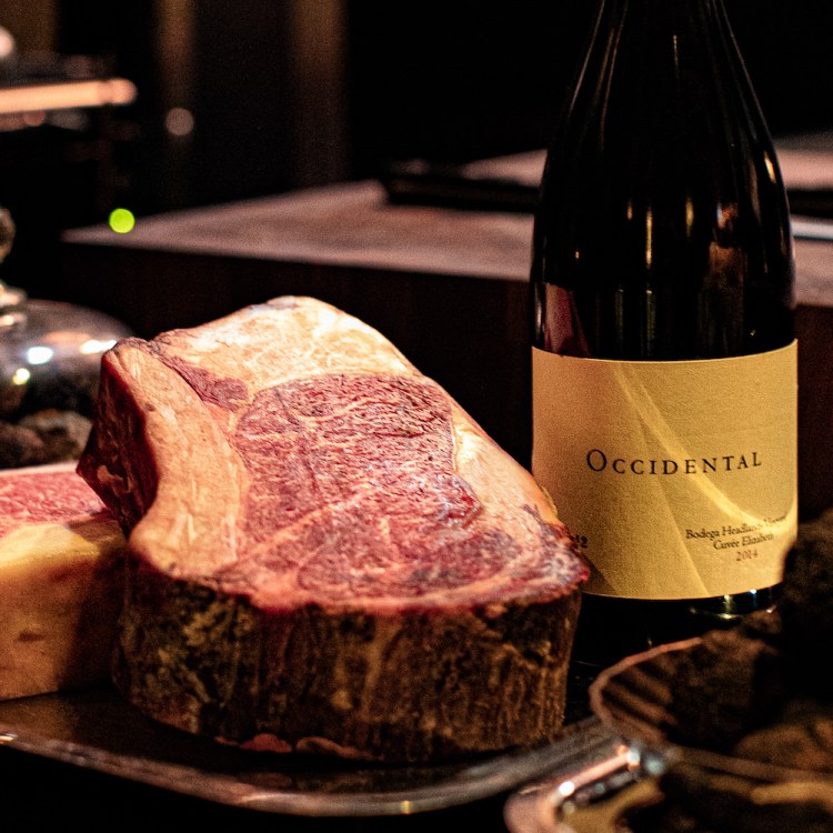 two thick steaks on a silver tray next to a bottle of red wine