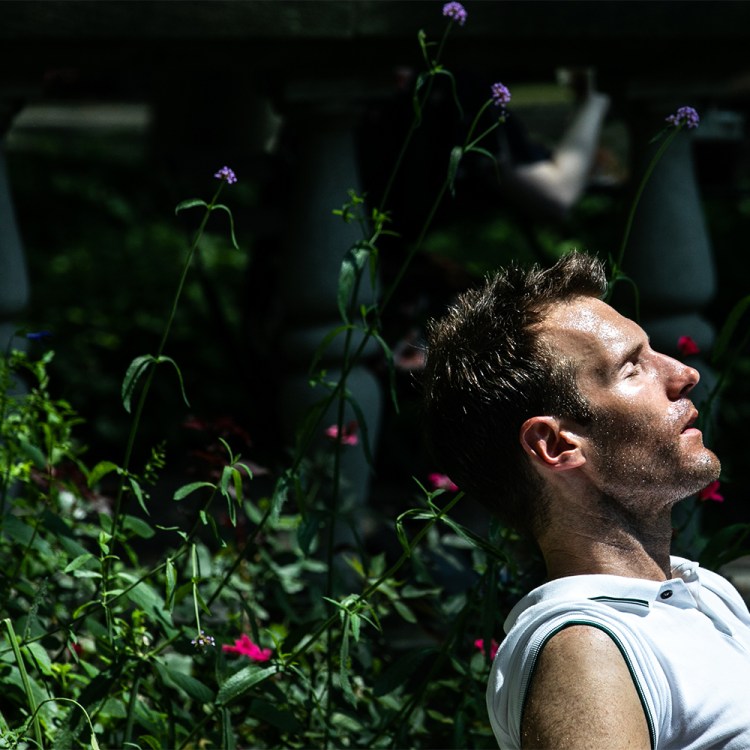 Man sitting in sunlight with eyes closed, reflecting in a quiet garden.